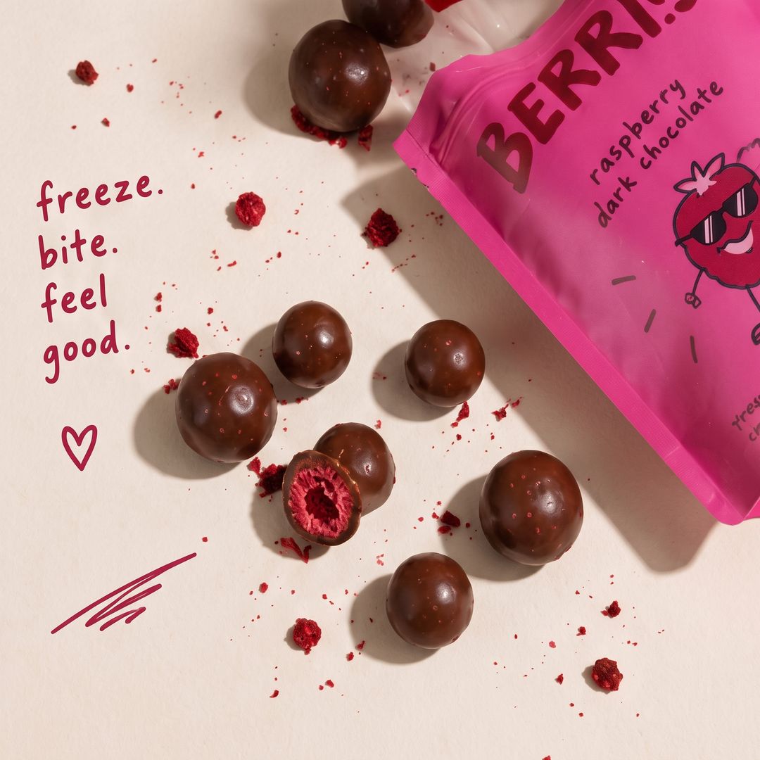 Chocolate-covered raspberries scattered on a table, one bitten open to show the fruit.